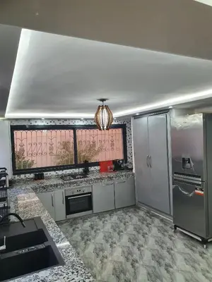 a kitchen with white cabinets and a large window at Villa entière in Azemmour