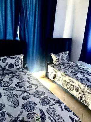 two beds in a room with blue curtains at Mohammed V Airport Appartement in Deroua