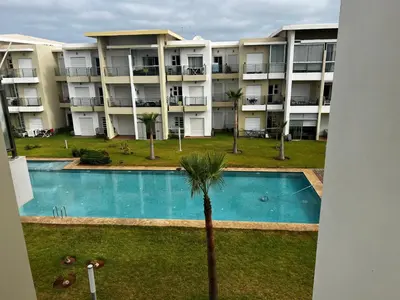 an apartment building with a swimming pool and a palm tree at Appartement de vacances CASABAY Sidi Rehal in Sidi Rahal