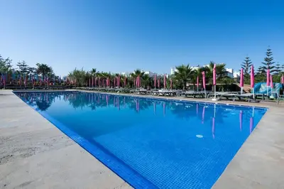 a large swimming pool with blue water and palm trees at Résidence Luxe avec Plage Privée in Bouznika