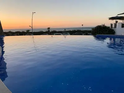 a large blue swimming pool with a sunset in the background at Résidence beach house in Dar Bouazza