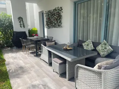 a patio with wicker chairs and a table and tables at Eden Island Bouznika Bel appartement avec jardin in Bouznika