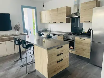 a kitchen with wooden cabinets and a large island with bar stools at Eden Island Bouznika Bel appartement avec jardin in Bouznika