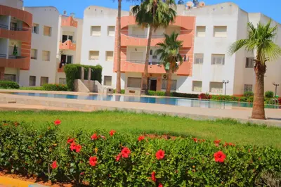 a courtyard of a building with red flowers and palm trees at Mohammedia 2 in Mohammedia