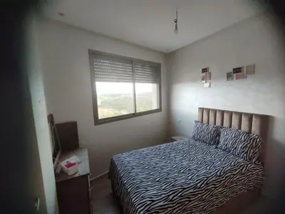 a bedroom with a bed with a striped comforter and a window at appartement jinane in Bouznika