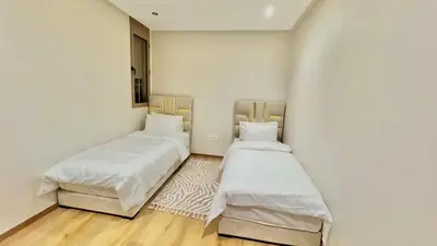 two beds in a room with white walls and wooden floors at T1 App moderne 2 chambres, a 10 min du Stade Moulay Abdellah in Temara