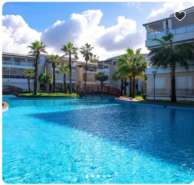 a swimming pool in front of a building with palm trees at Les perles de tamaris in Dar Mohammed Ould Haj Jilali