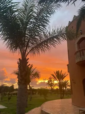 a palm tree next to a building with a sunset at Bienvenue au Château Loriana ! in Bouznika