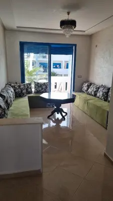 a living room with a table and a couch at Bel Appartement avec Piscine et Jardin, EL MANSOURIA in Mansouria