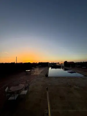 a sunset with a table and chairs next to a body of water at Casa Jnane Jawhara Skhirat in Rabat
