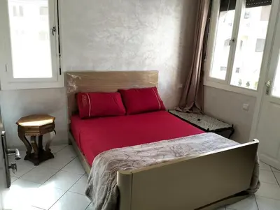 a bedroom with a bed with red sheets and two windows at kkjkbjbjb in Mohammedia