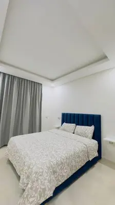 a white bedroom with a bed with a blue headboard at Cosy Suite Appart in Kasba Bou Hamira