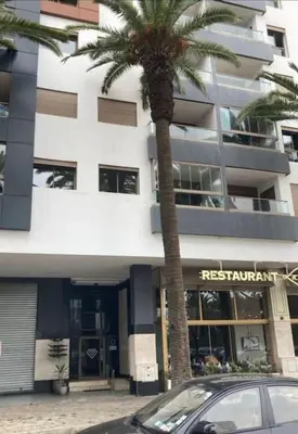 a car parked in front of a building with a palm tree at Apparemment 300 m de la plage, Parc Mohammedia in Mohammedia