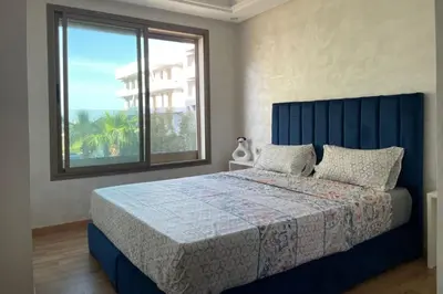 a bedroom with a blue bed and a large window at Garden Paradise Bouznika Beach Apartment in Bouznika