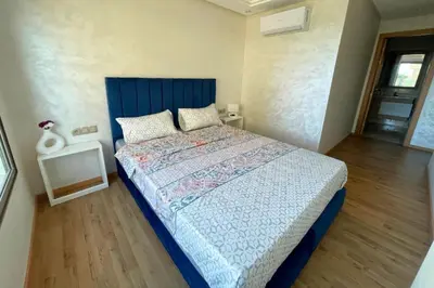 a bedroom with a large bed with a blue headboard at Garden Paradise Bouznika Beach Apartment in Bouznika