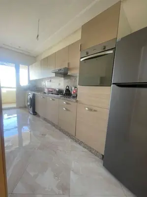 a kitchen with wooden cabinets and a stainless steel refrigerator at Appart avec Piscine Proche de la Mer in Bouznika