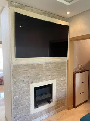 a brick fireplace with a large television on top of it at Appart avec Piscine Proche de la Mer in Bouznika
