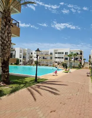 a resort with a swimming pool and a palm tree at Appartement vues piscine in Mansouria