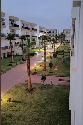 a view of a park with palm trees and a building at Appartement vues piscine in Mansouria