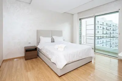 a white bedroom with a bed and a large window at Appartement géant in Rabat