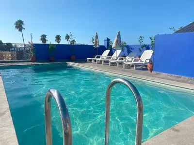 a swimming pool with chairs and a blue wall at Hôtel Les Remparts in Azemmour