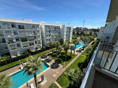 an apartment with a pool and palm trees and buildings at Sublime appart piscines & espaces jeux, proche mer in Bouznika