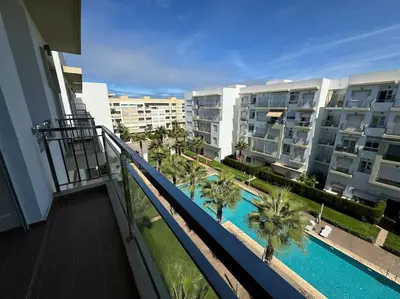 a balcony of a building with a pool and palm trees at Sublime appart piscines & espaces jeux, proche mer in Bouznika
