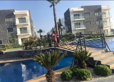 a woman walking over a bridge over a pool in front of a building at Superbe Appartement pieds dans l'eau - Résidence GARDENBAY in Dar Mohammed Ould Haj Jilali