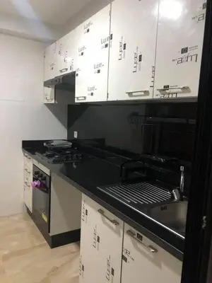 a kitchen with white cabinets and a black counter top at Superbe Appartement pieds dans l'eau - Résidence GARDENBAY in Dar Mohammed Ould Haj Jilali
