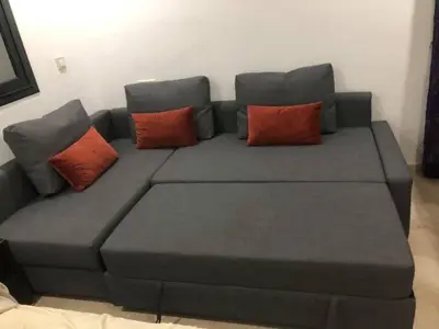 a gray couch with two red pillows on it at Superbe Appartement pieds dans l'eau - Résidence GARDENBAY in Dar Mohammed Ould Haj Jilali