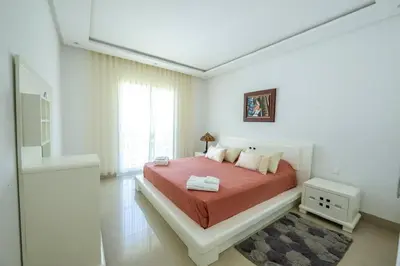 a white bedroom with a bed with a red blanket at Ocean Pearl - Exclusive 2BR Oceanfront Luxury & Views in Bouznika