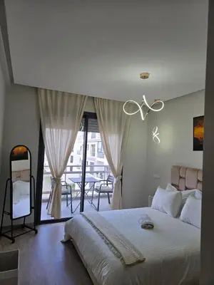 a bedroom with a large white bed and a balcony at Charmant appartement à 10min de L' Aéroport Med V in Nouaceur