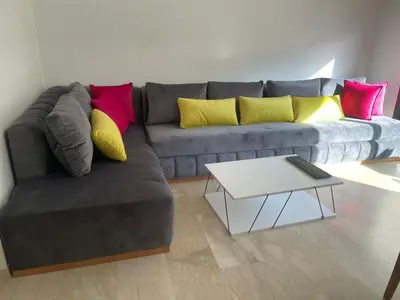 a living room with a gray couch with colorful pillows at Superbe Appartement pieds dans l'eau Résidence Garden Bay in Sidi Rahal