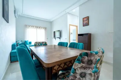 a dining room with a wooden table and blue chairs at Appartement avec Piscine Proche Plage in Bouznika