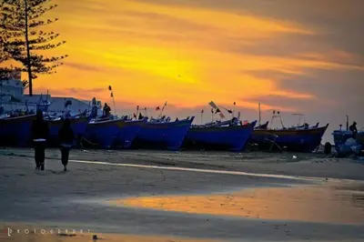 a group of boats on a beach with a sunset at Appartement neuf tres calme balcon vue sur l'océan in Skhirat