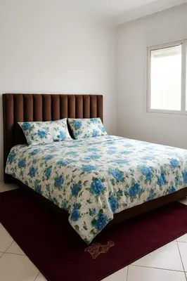 a bed with a blue and white comforter and a window at Dar wifak in Temara