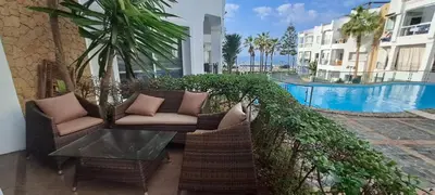 a patio with two chairs and a table next to a pool at Appartement Beach House 2 Dar Bouazza in Dar Bouazza
