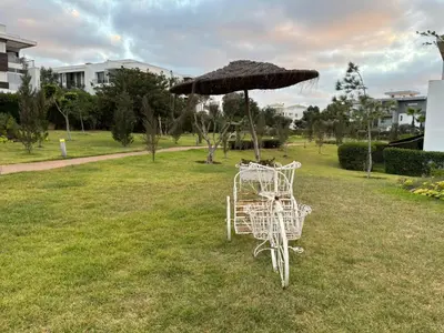 a white chair and an umbrella in a park at Bouskoura, appart jardin privé in Casablanca