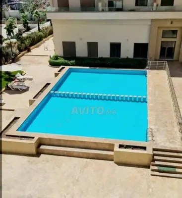 a large blue swimming pool in front of a building at Vue mer et parc, terrasse filante in Aïn Harrouda