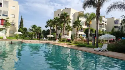 a swimming pool with palm trees and buildings at Les Perles de Bentriaa Mohammedia in Mohammedia