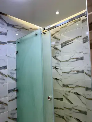 a glass shower door in a bathroom with marble walls at Cosy chambre salon à 2 min harhoura in Temara