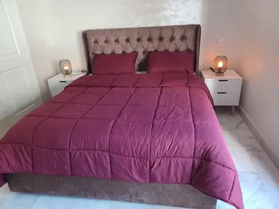 a bed with a purple comforter and two night stands at Lovely & Comfy Long and Short Stay at Nouacer-Casa 2-Bedroom Apartment in Nouaceur