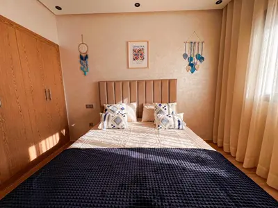 a bedroom with a large bed with blue and white pillows at Appartement Vue Mer & Coucher de Soleil in Aïn Harrouda