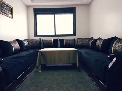 a living room with a black couch with a table at Logement cozy in Oulad Kerroum