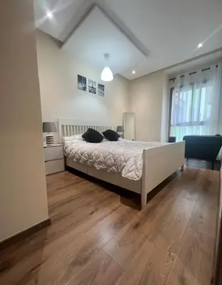a bedroom with a large bed and a wooden floor at Neuf 3min de la plage au parc avec parking in Mohammedia