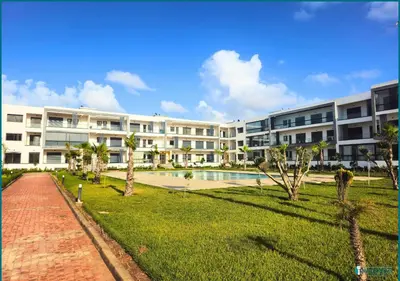 a large apartment building with a pool and palm trees at Une petite parenthèse marine in Mansouria