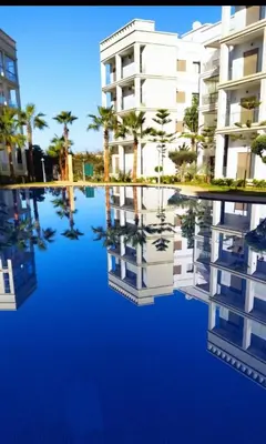 a view of a building with palm trees in the water at Charming Flat with Pool view Fast Wi-Fi in Bouznika