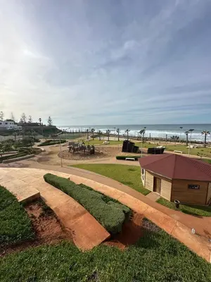 a park near the beach with a building and the ocean at Peninsula Dar Bouazza in Tamaris