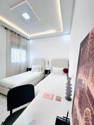a bedroom with two beds and a table with a vase at Elegant 3BR Stay 5min to Hay Riad in Temara