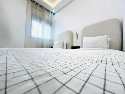 a white bed in a white room with a window at Elegant 3BR Stay 5min to Hay Riad in Temara